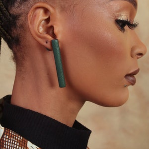 May include: A close-up of a person's ear with a long, dark green rectangular earring. The earring is made of wood and has a smooth, polished finish.
