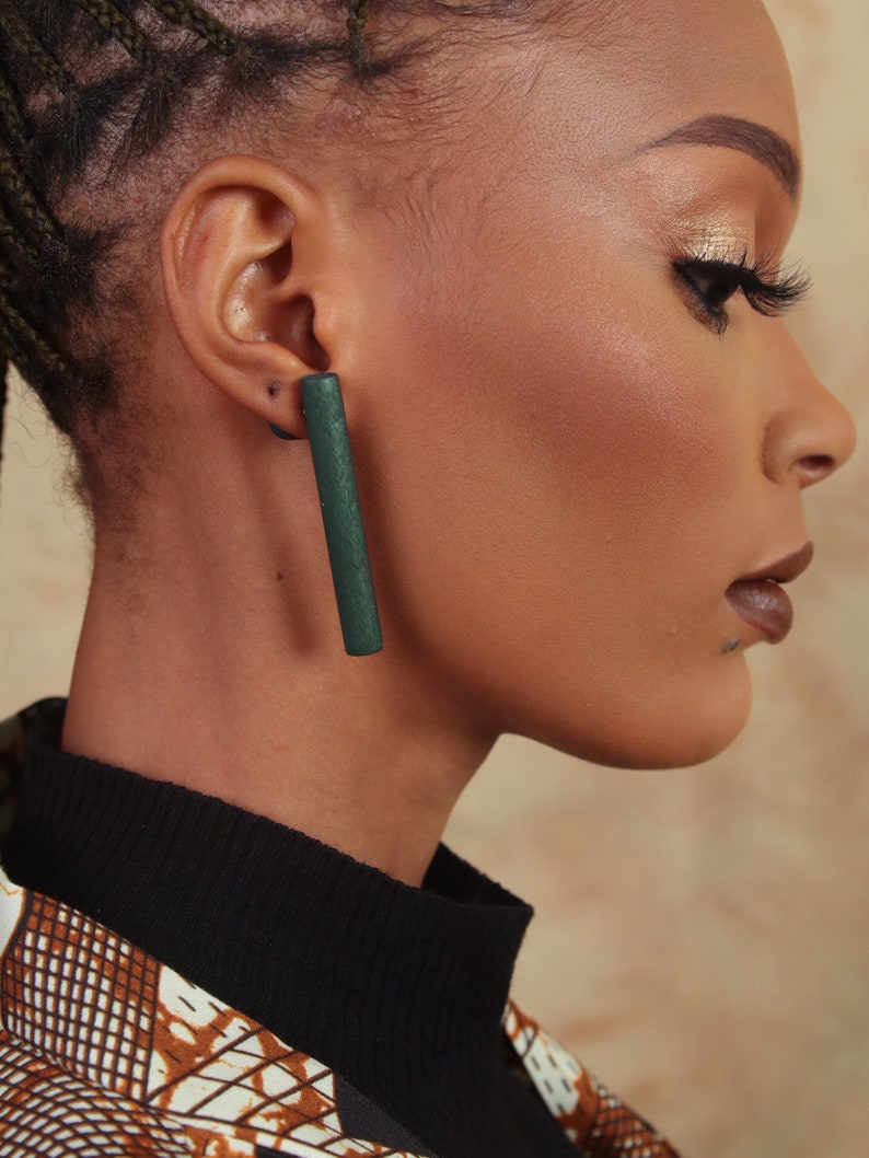 May include: A close-up of a person's ear with a long, dark green rectangular earring. The earring is made of wood and has a smooth, polished finish.
