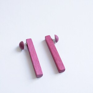 May include: A pair of pink wooden earrings with a simple rectangular shape. The earrings are made of wood and have a smooth finish.