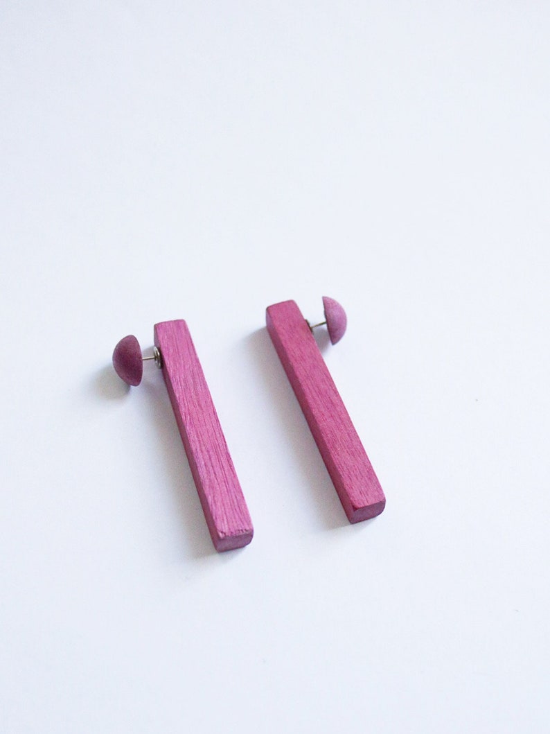 May include: A pair of pink wooden earrings with a simple rectangular shape. The earrings are made of wood and have a smooth finish.