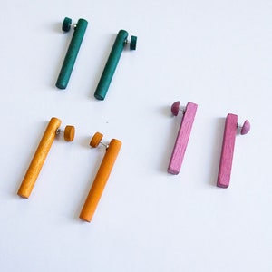 May include: Set of six wooden earrings in green, orange, and pink. The earrings are all rectangular in shape and have a simple design.