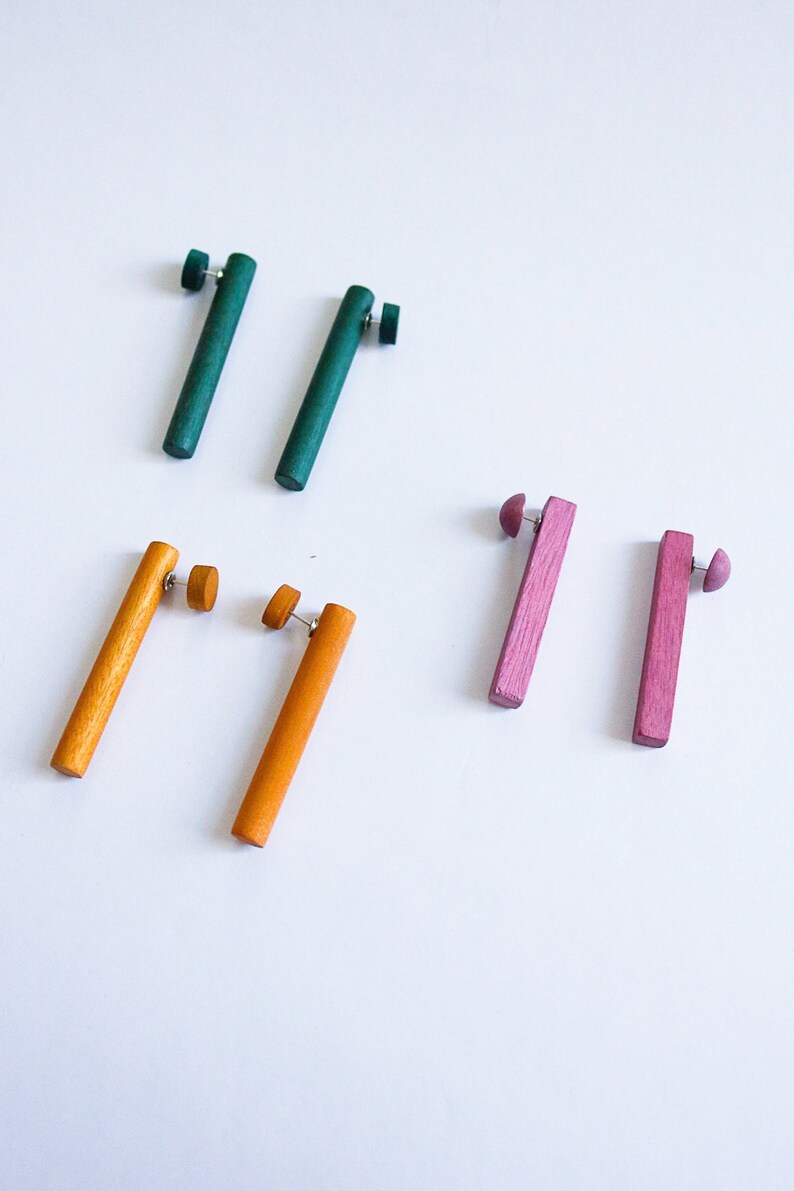 May include: Set of six wooden earrings in green, orange, and pink. The earrings are all rectangular in shape and have a simple design.
