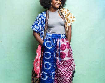 Könnte beinhalten: Eine Frau trägt ein graues Tanktop, einen farbenfrohen Kimono und eine weite Hose. Der Kimono hat blaue, rosa und gelbe Muster. Die Hose ist blau und rosa mit geometrischen Designs. Sie lächelt und trägt goldene Creolen.