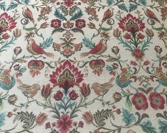 May include: A beige fabric with a repeating pattern of red, brown, and green floral designs and birds. The fabric has a woven texture.