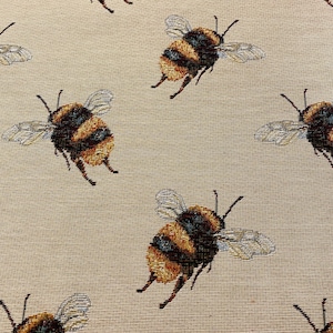 May include: A beige fabric with a repeating pattern of brown and yellow bumblebees. The bees are depicted in a realistic style with detailed wings and bodies.