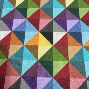 Könnte beinhalten: Ein farbenfroher geometrischer Musterstoff mit einem sich wiederholenden Muster aus Dreiecken in Rot-, Orange-, Gelb-, Grün-, Blau-, Lila- und Grautönen.