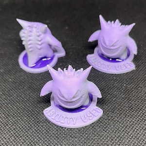 May include: Three purple 3D printed figurines of a Pokemon character, Gengar, with a purple base that reads "Ability Used".