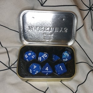 May include: A set of blue dice with white numbers in a metal tin with the text "BYKKIEX?" on the lid.