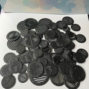 May include: A collection of various sized black circular vent covers with different patterns. The vents have a series of parallel lines, cross-hatched designs, and other geometric patterns. The vents are made of a matte black material.