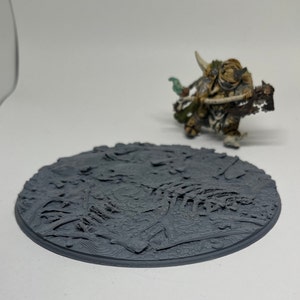 May include: A gray plastic miniature gaming base with a textured surface resembling a rocky terrain. The base is designed for use with tabletop games and miniature figures.