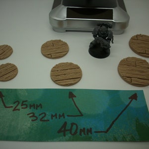 May include: A set of six wooden round bases for miniature figures. The bases are 25mm, 32mm, and 40mm in diameter. The bases are painted in a light brown color and have a wood grain texture.