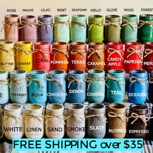 May include: A collection of 36 mason jars painted in various colors, including rose, mauve, lilac, mint, seafoam, kelly, olive, moss, forest, butter, canary, coral, pumpkin, terra, caramel, candy apple, paprika, merlot, ice, tiffany, aqua, carolina, denim, coastal, teal, dodger, navy, clear lit, white, linen, sand, smoke, slate, nutmeg, espresso, and black. The jars are arranged in four rows of nine jars each. The jars are all the same size and shape, and they are all decorated with a simple brown ribbon tied around the neck.