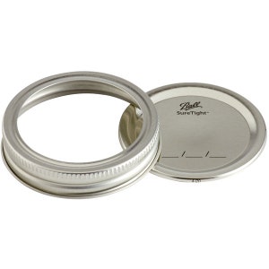 May include: Two silver metal canning lids, one with a Ball SureTight label and a blank space for writing a date.