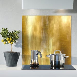 May include: A kitchen scene featuring a small potted lemon tree with yellow fruit, a stainless steel stovetop espresso maker, and a stainless steel pot. A large gold-colored panel is in the background.
