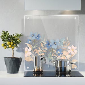 Könnte beinhalten: Eine transparente Küchenrückwand aus Glas mit einem floralen Design in Blau und Rosa. Ein Kochtopf und eine Espressomaschine aus Edelstahl stehen auf einem schwarzen Kochfeld. Ein Topf mit Zitrusbaum und gelben Früchten steht auf der Theke.