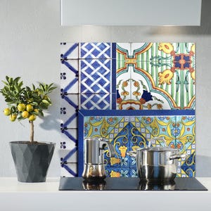 Op de afbeelding: Een keukenachterwand met een kleurrijk tegelontwerp in blauw, groen, geel en rood. De achterwand bevindt zich achter een fornuis met een koffiepot en een pan.