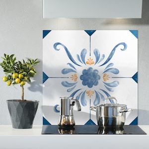 Puede incluir: Un protector de salpicaduras de cocina blanco con un diseño floral azul y naranja. Una olla de plata y una cafetera de plata están sobre una estufa negra.