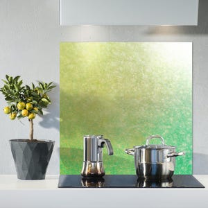 Könnte beinhalten: Eine Küchenszene mit einem kleinen Topf-Zitronenbaum mit gelben Früchten, einem Espressokocher aus Edelstahl und einem abgedeckten Edelstahltopf. Eine grüne und gelbe abstrakte Rückwand befindet sich hinter den Geräten.