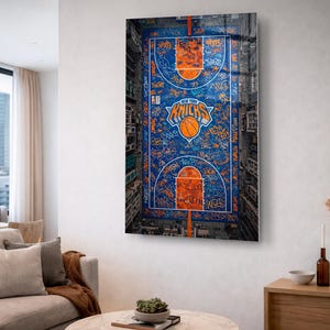 Może przedstawiać: Oprawiony wydruk przedstawiający z lotu ptaka boisko do koszykówki z logo New York Knicks i piłką. Boisko jest pomalowane na niebiesko i pomarańczowo z graffiti.