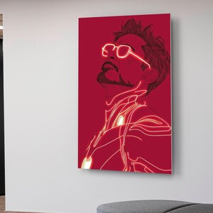 Puede incluir: Una impresi&oacute;n en lienzo roja que presenta una ilustraci&oacute;n estilizada de un hombre mirando hacia arriba. La obra de arte utiliza una combinaci&oacute;n de colores rojo y blanco, con l&iacute;neas blancas brillantes que delinean la figura y las gafas. El arte est&aacute; montado en una pared blanca.