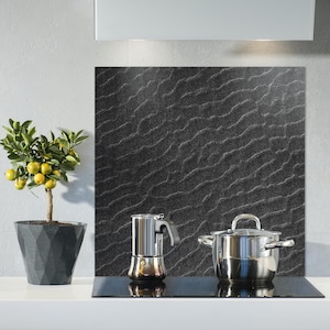 May include: A kitchen scene featuring a small potted lemon tree with yellow fruit, a stainless steel stovetop, a silver coffee maker, and a stainless steel pot. The background has a black textured backsplash.