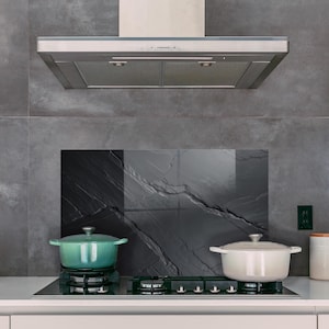 Puede incluir: Una cocina moderna con una campana extractora de acero inoxidable sobre una placa de gas. Una olla de color turquesa está en el quemador, junto a una olla blanca. También se ven una tetera blanca y botes con tapas de madera.