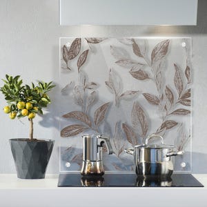 Könnte beinhalten: Küchenszene mit einer Glas-Rückwand mit braunem Blättermuster. Ein Edelstahl-Topf und eine Espressomaschine stehen auf einem schwarzen Kochfeld. Ein kleiner Topf mit Zitrusfrüchten mit gelben Früchten.