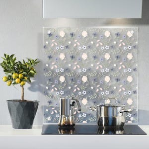 May include: A kitchen setting with a floral patterned splashback featuring blue, pink, and white flowers. A stainless steel pot and coffee maker are on a black hob. A potted lemon tree with yellow fruit is on the counter.
