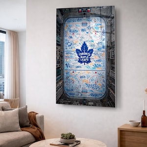 Peut inclure: Impression d'art encadrée représentant une vue aérienne d'une patinoire de hockey. L'œuvre présente le logo et le texte bleu des Maple Leafs de Toronto, avec un style graffiti sur la glace. L'impression est exposée dans un salon moderne.