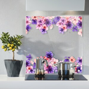 Könnte beinhalten: Eine Küchenszene mit einer Glasrückwand mit floralem Design in Lila- und Rosatönen. Ein Edelstahl-Kochtopf und eine Espressomaschine stehen auf einem schwarzen Kochfeld. Links steht ein Zitronenbaum im Topf.