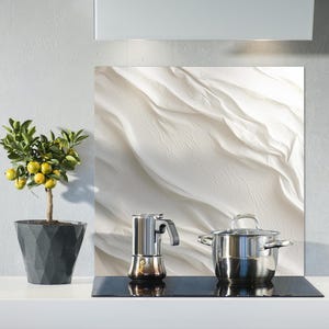 Könnte beinhalten: Eine weiße Küchenrückwand mit einem wellenförmigen, abstrakten Design. Eine silberne Kaffeekanne und ein silberner Topf stehen auf einem schwarzen Kochfeld.