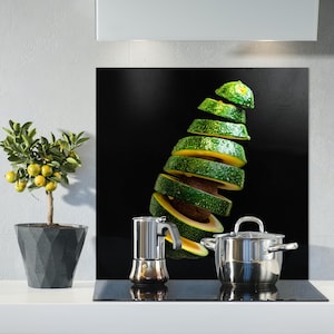 Puede incluir: Un protector de salpicaduras de cocina de vidrio negro con un aguacate verde cortado en rodajas finas, una olla de plata con asa y una cafetera de plata.