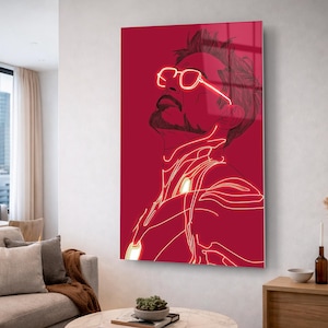 Puede incluir: Una impresi&oacute;n de arte mural roja que presenta una ilustraci&oacute;n estilizada de un hombre con gafas, delineada con l&iacute;neas de ne&oacute;n. La obra de arte est&aacute; montada en una pared en un sal&oacute;n moderno, con muebles y decoraci&oacute;n de tonos neutros.