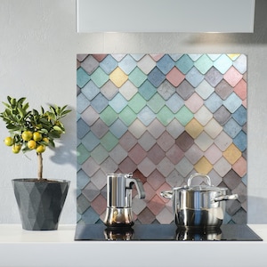 May include: A kitchen scene featuring a decorative backsplash with a colorful diamond pattern. A stainless steel pot and espresso maker sit on a black stovetop. A potted lemon tree with yellow fruit adds a natural element.
