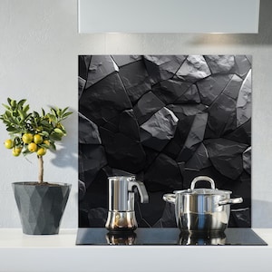 May include: A kitchen scene featuring a black stone backsplash, a stainless steel pot and a stovetop espresso maker. A small potted lemon tree with yellow fruit is on the left. The scene is set against a white wall.