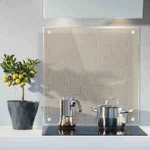 Könnte beinhalten: Eine moderne Küche mit einer Glasrückwand mit einem geometrischen Muster in Gold. Ein silberner Topf und eine silberne Kaffeemaschine stehen auf einem schwarzen Elektroherd.