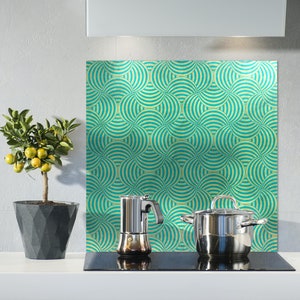 May include: A kitchen backsplash with a teal and yellow geometric pattern. A silver coffee pot and a silver pot with a black handle are on a black stovetop.