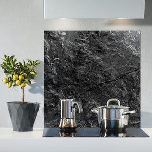 Puede incluir: Una escena de cocina con un pequeño limonero en maceta con frutos amarillos, una cafetera exprés de acero inoxidable y una olla cubierta de acero inoxidable. Una placa para salpicaduras negra y gris con aspecto de piedra está detrás de los electrodomésticos.