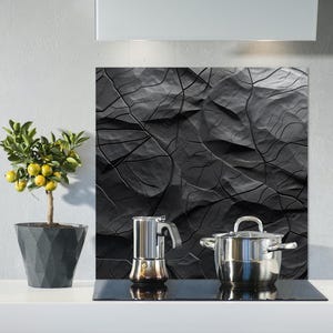 May include: A kitchen scene featuring a small potted lemon tree with yellow fruit, a stainless steel stovetop, and a black textured backsplash. A stainless steel coffee maker and a pot with a lid are on the stovetop.
