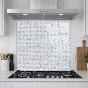 May include: A square kitchen splashback panel featuring a mosaic pattern of small, individual tiles in varying shades of white, light grey, and dark grey. The panel is positioned behind a black gas hob and beneath a stainless steel cooker hood.