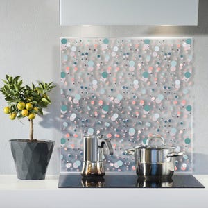 Könnte beinhalten: Eine Küchenszene mit einem kleinen Topf-Zitronenbaum mit gelben Früchten, einem Espressokocher aus Edelstahl und einem Topf mit Deckel. Eine dekorative Glas-Rückwand mit farbigem Punktmuster befindet sich hinter den Geräten.