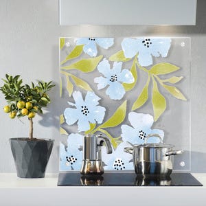 May include: A kitchen setting with a floral glass splashback in light blue and green. A small potted citrus tree with yellow fruit is on the left. A stainless steel pan and coffee maker sit on the hob.