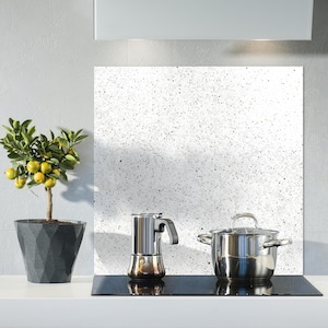 May include: A kitchen scene with a small potted lemon tree bearing yellow fruit, a stainless steel stovetop espresso maker, and a stainless steel pot with a lid. The background has a white speckled backsplash.