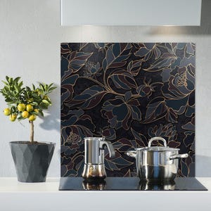 May include: A black and gold floral patterned glass backsplash for a kitchen or stovetop. The backsplash is decorated with a repeating pattern of stylised flowers and leaves.