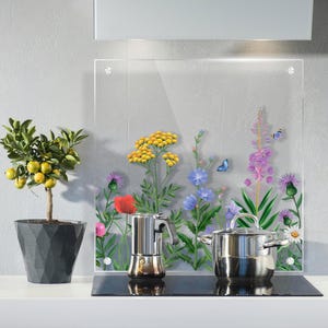 Könnte beinhalten: Eine transparente Küchenrückwand aus Glas mit einem Blumendesign mit gelben, lila und blauen Wildblumen. Ein Edelstahltopf und eine Espressomaschine stehen auf einem schwarzen Kochfeld. Ein Topf mit Zitrusbaum steht links.