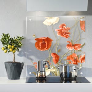 Könnte beinhalten: Eine transparente Küchenrückwand aus Glas mit einem Blumendesign aus roten und weißen Mohnblumen. Ein Kochtopf aus Edelstahl und eine Kaffeemaschine stehen auf dem schwarzen Kochfeld. Ein Topf mit Zitrusbaum steht links.