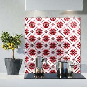 May include: A white kitchen backsplash with a red and black geometric pattern. A silver coffee pot and a silver pot with a black handle are on a black stovetop.