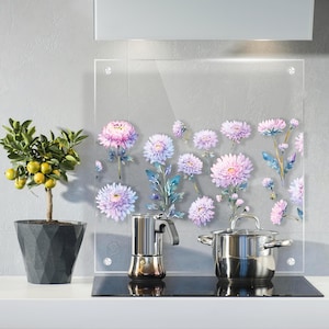 以下が含まれることがあります： ピンクと紫の花柄がデザインされた透明なガラス製のキッチンバックボード。ステンレス製の鍋とエスプレッソメーカーが黒いコンロの上にあります。黄色い実の小さな鉢植えの木がカウンターにあります。