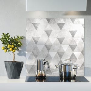 Könnte beinhalten: Eine Küchenszene mit einem kleinen Topf-Zitrusbaum mit gelben Früchten, einem Espressokocher aus Edelstahl und einem abgedeckten Edelstahltopf. Im Hintergrund befindet sich eine geometrische Fliesenrückwand.