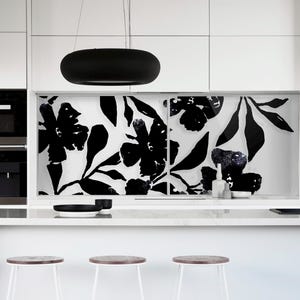 Könnte beinhalten: Moderne Küche mit weißen Schränken, einer Marmorarbeitsplatte und einem schwarzen Wasserhahn. Die Rückwand zeigt ein schwarz-weißes Blumenmuster. Über der Insel hängt eine schwarze Pendelleuchte, darunter Barhocker.